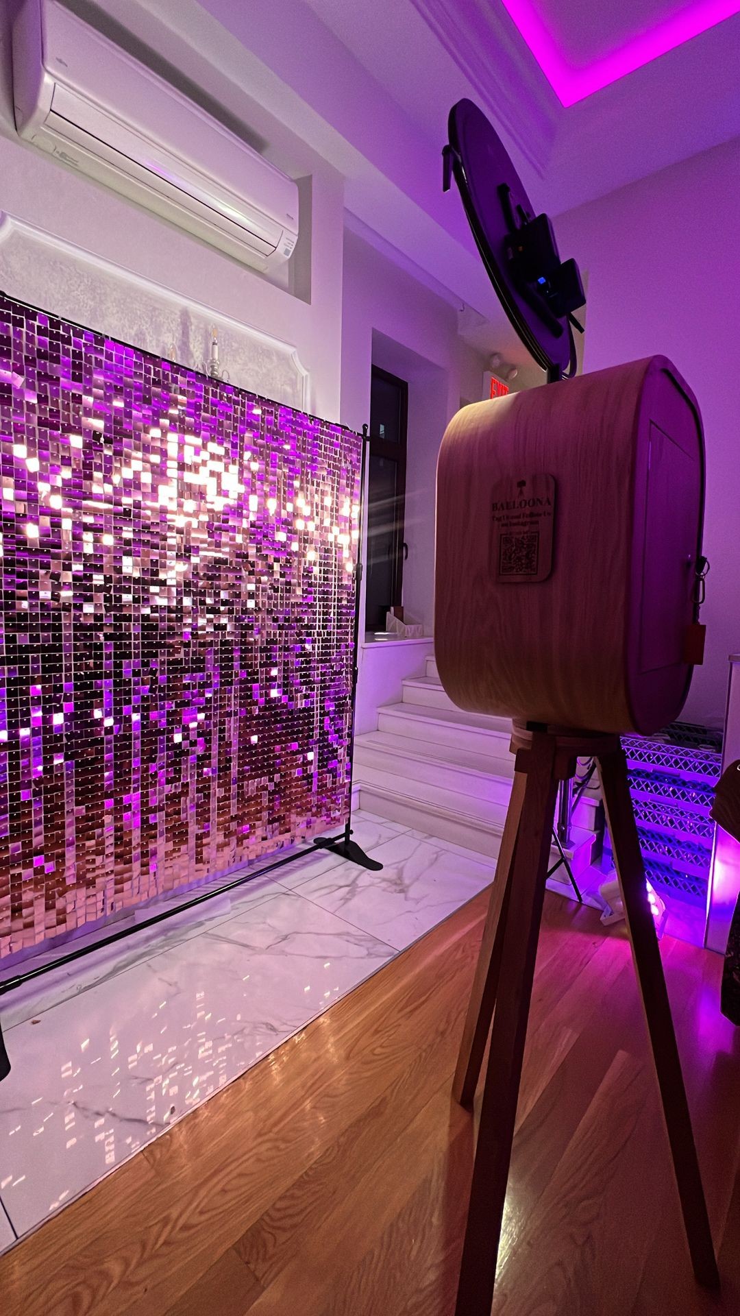 Photo booth setup with a sparkly purple sequin backdrop and vintage-style camera in dim lighting.